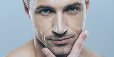 Attraktiver Mann schaut in Kamera und hält sein Kinn zwischen Daumen und Zeigefinger